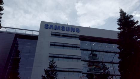 Samsung-Research-America-SRA-campus-in-Silicon-Valley-bottom-up-view-with-green-pine-trees-landscape-under-overcast-sky