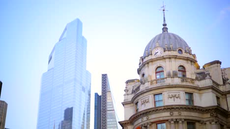 Bank-Station-in-downtown-London,-tilting-up-stone-city-buildings,-monument-and-sky-scrapers,-red-double-decker-bus-passing-by