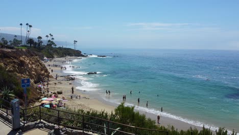 Laguna-Beach-CA-USA,-Aerial-View-of-People-on-Sandy-Shore-on-Hot-Sunny-Day,-Revealing-Drone-Shot