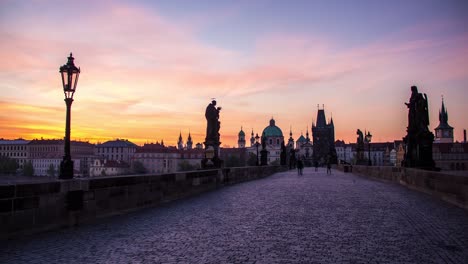 Night-to-day-sunrise-timelapse-of-the-Charles-Bridge-in-Prague,-Czech-Republic-with-a-view-of-the-Old-Town,-statues,-lamps-and-the-cobblestones-on-the-bridge-as-the-blue-sky-turns-to-colorful-gold