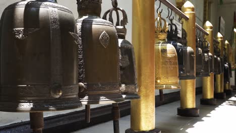 Row-of-Buddhist-temple-bells-hanging-from-golden-beam-with-their-clappers-moving-due-to-mild-wind-at-Wat-Phra-That-Doi-Suthep,-one-of-the-most-famous-temple-in-Chiang-Mai