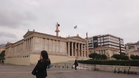 Establishing-shot,-People-walking-around-the-Academy-of-Athens,-Athena-Statue-in-the-background