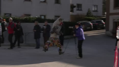 Young-man-in-mask-with-horn-running-down-street,-chasing-people-as-part-of-carnival