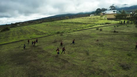 Group-of-African-children-playing-and-running-away-though-green-field-in-mountain-jungle-village-in-Tanzania-parallax-following-drone-shot