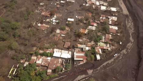 Drone-shot-showing-San-Miguel-Los-Lotes,-tilt-up-following-the-path-of-Volcan-de-Fuego-pyroclastic-flow