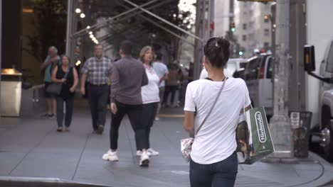 Woman-with-black-haur-in-white-T-shirt-carrying-food-and-Nindendo-bag-walking-down-the-Manhattan-street-in-slow-motion-in-New-York-City-during-daytime