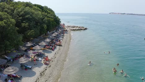 Aerial-forward-along-coast-and-beach-of-Croatian-island-with-tourists