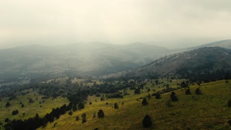 Imágenes-De-Drones-De-Las-Cimas-De-Una-Montaña-Brumosa,-Todo-Es-Verde-Y-La-Luz-Brilla-A-Través-De-Las-Nubes