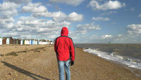 Man-walking-on-the-sand-along-the-shore-of-a-windy-beach-on-a-sunny-day,-slow-motion-shot