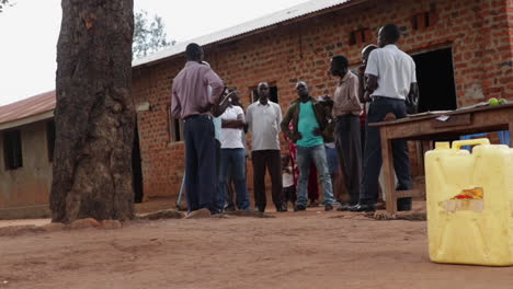 Grupo-De-Hombres-Ugandeses-En-Círculo-Hablando-Mientras-Están-Parados-Afuera-Del-Edificio-De-Ladrillo-En-Kampala,-Uganda