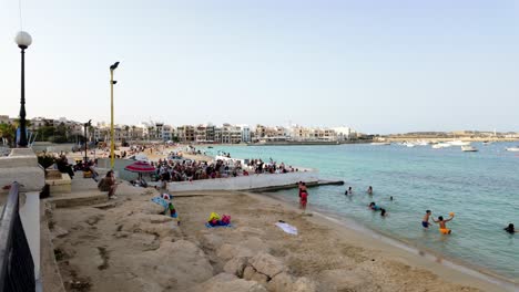 Relaxing-people-and-playing-kids-along-the-sandy-beach-of-Pretty-Bay-on-a-summer-day-in-Birzebbuga,-Malta