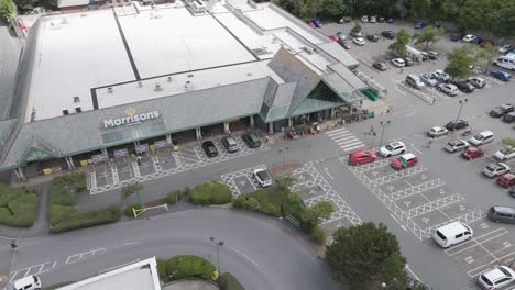 Drone-exterior-rising-view-of-Morrisons-supermarket-with-carpark-and-nearby-roads,-Bude,-Cornwall,-UK,-July-2024