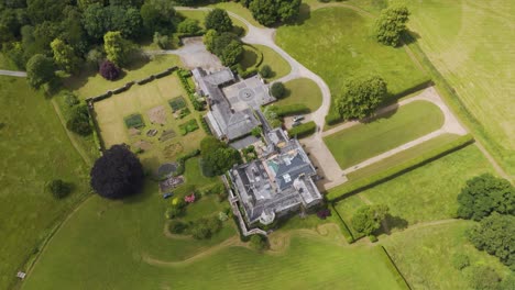 Drone-view-of-Grade-Two-Star-listed-Hayne-Manor-in-Devon,-UK,-captured-in-June-2024,-surrounded-by-lush-greenery-and-gardens