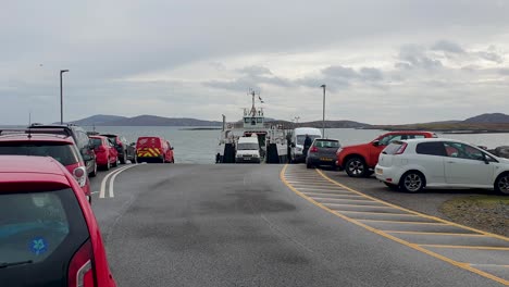 Vehicles-disembarking-inter-island-Caledonian-MacBrayne-ferry-and-rows-of-cars-waiting-to-board-in-remote-isles-of-Outer-Hebrides-in-Scotland-UK