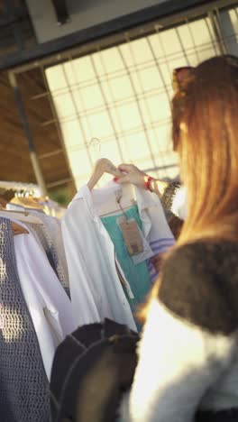 Chica-Eligiendo-Ropa-En-El-Mercado-De-Pulgas,-Moda-De-Ropa-Vintage-De-Segunda-Mano,-Video-Vertical