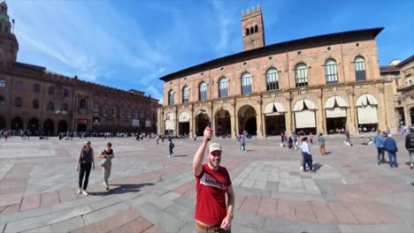 Male-tourist-holds-360-camera-above-head,-spinning-view-of-Piazza-Maggiore,-Bologna,-Italy
