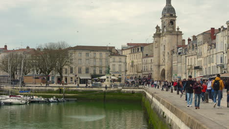 People-walking-along-the-historic-harbor-in-La-Rochelle,-France,-near-the-iconic-clock-tower