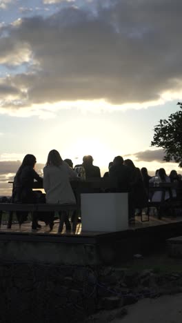 People-dining-at-table-outdoor,-socialising,-sun-backlight-at-sunset,-Vertical-video