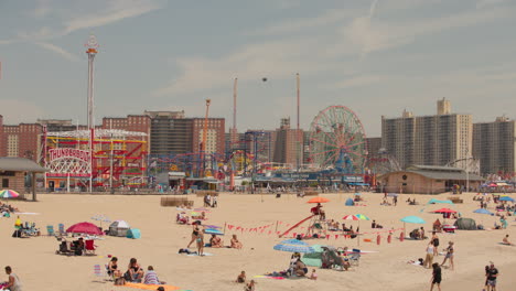 Coney-Island-Luna-Park-from-beach-in-the-summer,-people-relaxing,-New-York,-US