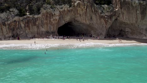 Aerial---coastal-mountain-with-cave-opening-near-turquoise-water,-Sardinia