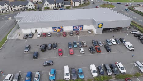 Aerial-orbital-of-a-Lidl-supermarket-in-Bude,-Cornwall,-United-Kingdom,-in-July-2024,-providing-a-comprehensive-view-of-the-supermarket's-exterior,-parking-spaces,-and-surrounding-neighborhood