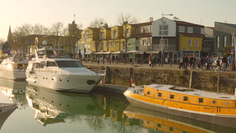 Pedestrians-stroll-along-the-waterfront-in-La-Rochelle's-Le-Gabut-district,-where-charming-Scandinavian-style-buildings-and-docked-boats-are-bathed-in-golden-sunlight