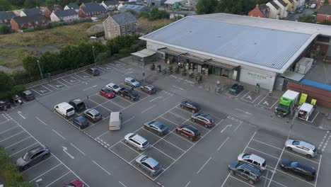 Aerial-establishing-view-of-Waitrose-supermarket-in-Holsworthy,-showing-the-building,-carpark,-and-adjacent-areas,-Devon,-United-Kingdom,-June-2024