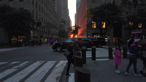 A-street-view-of-a-New-York-City-intersection-during-sunset,-the-sun-is-positioned-between-two-rows-of-tall-buildings