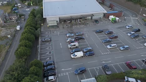 Drone-orbital-view-of-Waitrose-supermarket-and-carpark,-capturing-the-retail-environment-and-surrounding-areas,-Holsworthy,-Devon,-United-Kingdom,-June-2024