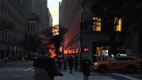 A-street-view-of-a-New-York-City-intersection-during-sunset,-the-sun-is-positioned-between-two-rows-of-tall-buildings