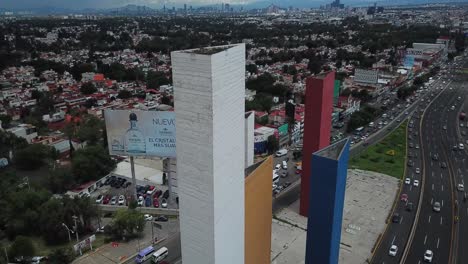 Orbital-drone-shot-with-the-"Torres-de-Satélite"-in-the-foreground-and-the-suburb-of-Ciudad-Satelite-on-the-outskirts-of-Mexico-City