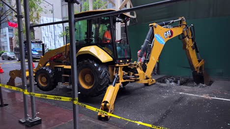 A-street-view-of-a-tractor-digging-a-hole-in-a-street-in-New-York-City-on-a-rainy-day