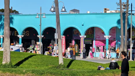 Stores-on-venice-beach-inside-a-blue-wall-facade-building-on-a-sunny-day-with-palm-trees-on-the-foreground