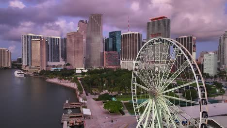 Marina-and-ferris-wheel-in-front-of-skyline-of-Miami-City-downtown-during-purple-colored-sky-at-sunset