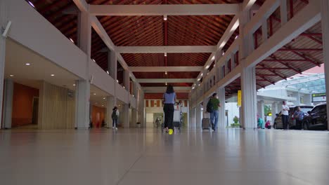 People-walking-through-a-modern-airport-terminal-with-luggage-carts-in-Bali-Indonesia