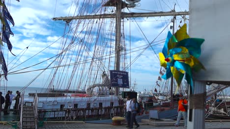 A-beautiful-red-and-yellow-pinwheel-spinning-at-a-harbor-in-slow-motion-4K-and-people-are-walking-behind-it-in