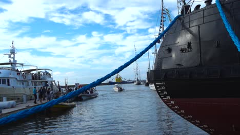 Footage-features-a-big-metallic-red-and-black-navy-boat-or-a-ship-in-Tallinn-harbor-at-a-festival-tied-down-with-vibrant-big-blue-ropes