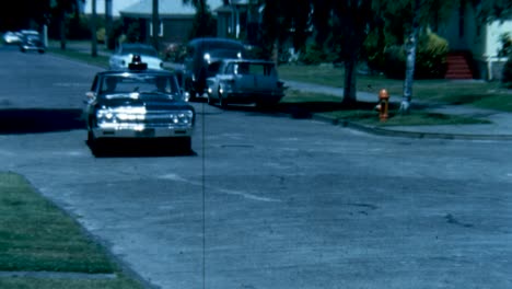 Coche-De-Policía-De-Los-Años-60-Circulando-Por-Una-Calle-Residencial