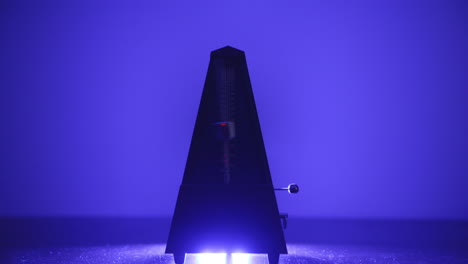 Metronome-that-is-moving-back-and-forth-that-is-lit-below-by-a-blue-light