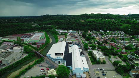 Aerial-view-of-factories-and-homes-in-Pittsburgh,-Pennsylvania,-with-a-river-and-green-hills-under-a-cloudy-sky