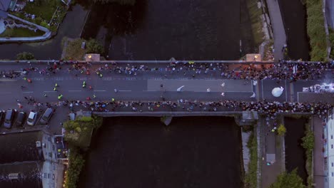 Descending-aerial-top-down-view-of-the-Pegasus-Parade-crossing-the-crowded-O'Brien's-Bridge-in-Galway