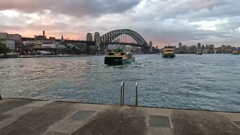 Sydney-Ferries-Bewegen-Sich-In-Anlegestellen-Am-Circular-Quay-Mit-Der-Sydney-Harbour-Bridge-Im-Hintergrund-In-Den-Frühen-Abendstunden