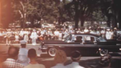 Un-Coche-Negro-Clásico-Y-Brillante-Atraviesa-Multitudes-En-Una-Ceremonia-Militar-En-Los-Años-1950