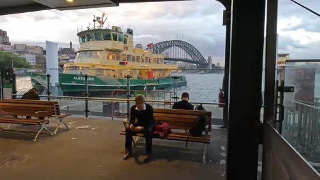 Passagiere-Warten-Am-Circular-Quay-Auf-Eine-Fähre-Am-Frühen-Abend-Mit-Der-Sydney-Harbour-Bridge-Dahinter