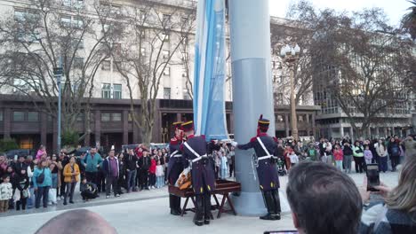 Oficiales-Militares-Argentinos-Bajan-La-Bandera-Nacional-En-El-Parque-Urbano-De-La-Independencia-Con-La-Gente-Local-Observando,-Panorámicas-A-La-Luz-Del-Día