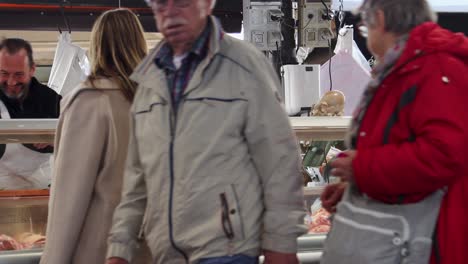 People-walk-by-meat-counter-at-food-market-in-Antibes,-France