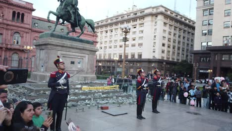 Military-officers-and-local-people-sightseeing-argentine-flag-lower-at-Pink-house,-independence-monument-at-winter-sunset