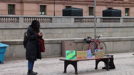 Lone-girl-stands-by-bench-with-climate-protest-placards-in-Stockholm