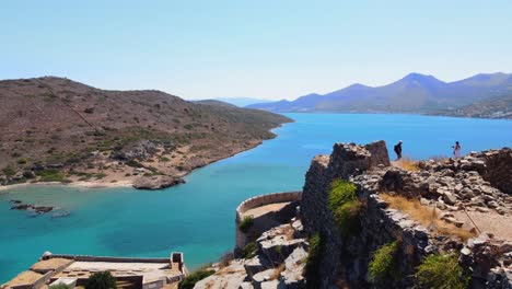 Revelando-La-órbita-Aérea-Sobre-El-Bastión-De-La-Fortaleza-Veneciana-De-Spinalonga-Y-Una-Pareja-De-Turistas-Explorando,-Creta,-Grecia