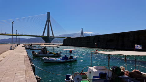 Impresionante-Vista-Desde-Los-Barcos-En-El-Agua-Turquesa,-Hasta-El-Puente-Del-Río-En-Un-Día-Soleado-De-Cielo-Azul,-Grecia